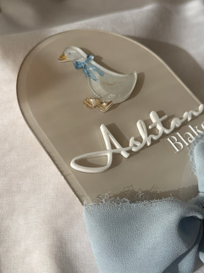 Decorative item with a duck design and 'Ashley' text on a beige background