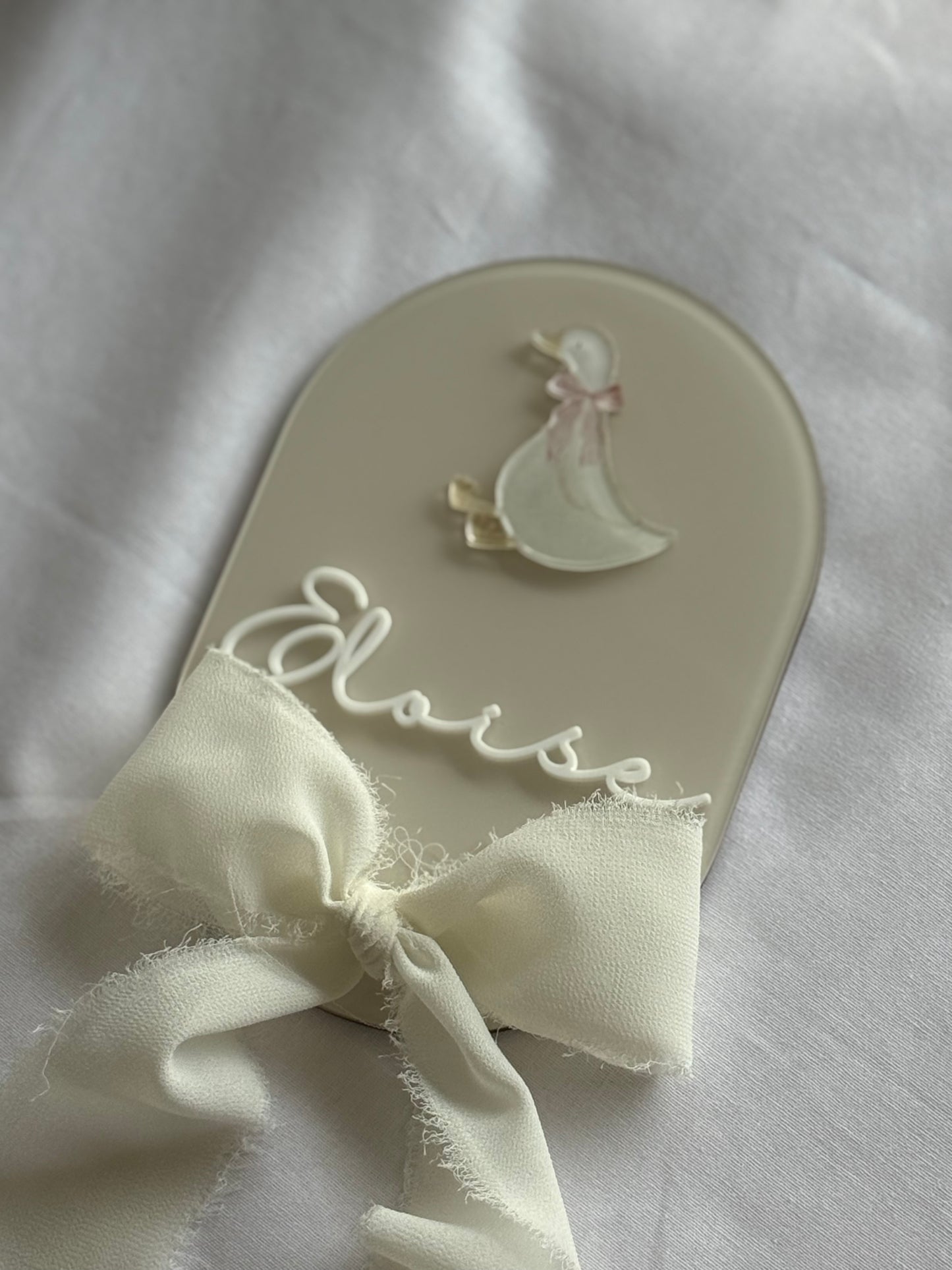 Decorative spoon with a bow and 'Elise' engraving on a white fabric background