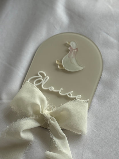 Decorative spoon with a bow and 'Elise' engraving on a white fabric background